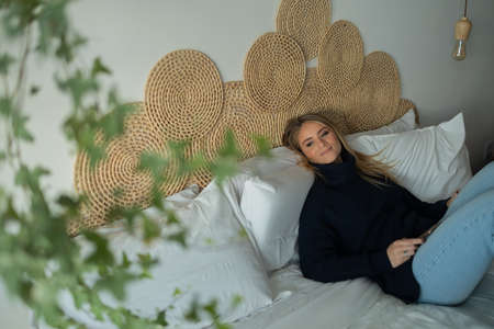 Young woman listening to music with headphones in her ears in her bed in her bedroom inside her apartment. High quality photo. Mobile phone, technology, music, urban living, feel good concept.の写真素材