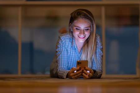 Young woman using a smartphone at night time with city view landscape in the background. High quality photo. photo. Mobile phone, technology, urban concept.の写真素材