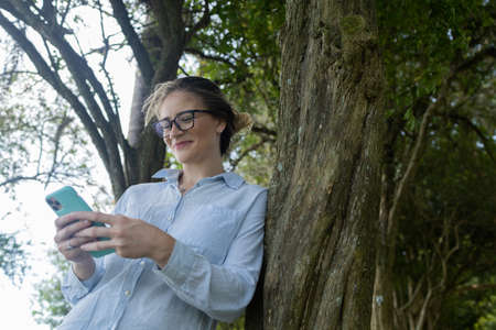 Young woman using a smartphone at day time with a green park in the background. High quality photo. Mobile phone, technology, urban concept. high quality photoの写真素材
