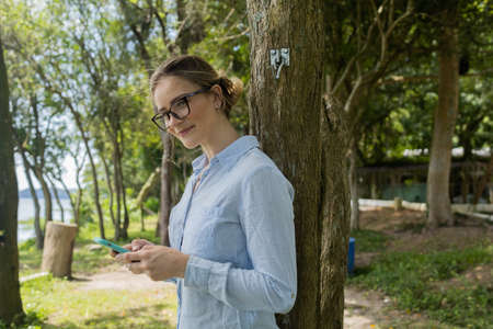 Young woman using a laptop at day time with a green park in the background. High quality photo. Mobile phone, technology, urban concept.の写真素材