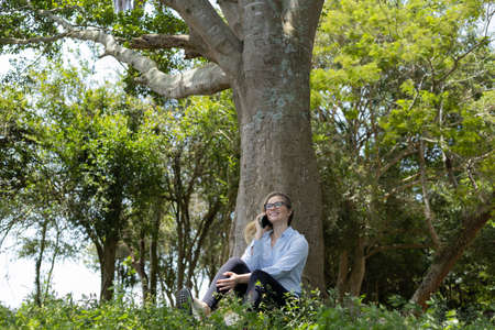 Young woman using a laptop at day time with a green park in the background. High quality photo. Mobile phone, technology, urban concept.の写真素材