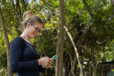 Young woman using a laptop at day time with a green park in the background. High quality photo. Mobile phone, technology, urban concept.の写真素材