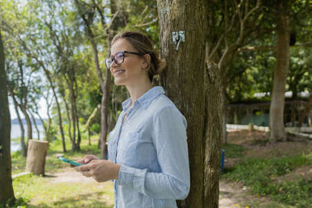 Young woman using a laptop at day time with a green park in the background. High quality photo. Mobile phone, technology, urban concept.の写真素材
