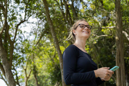 Young woman using a laptop at day time with a green park in the background. High quality photo. Mobile phone, technology, urban concept.の写真素材
