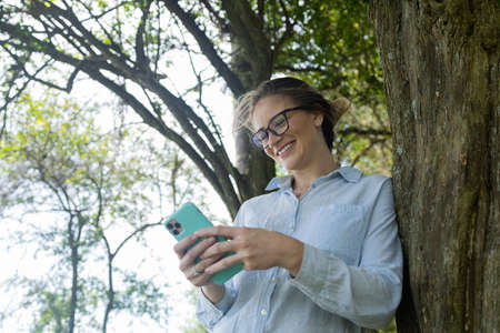 Young woman using a smartphone at day time with a green park in the background. High quality photo. Mobile phone, technology, urban concept. high quality photoの写真素材