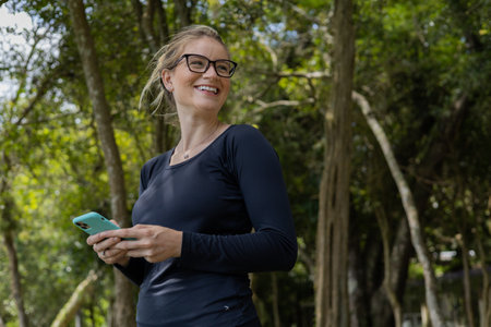 Young woman using a smartphone at day time with a green park in the background. High quality photo. Mobile phone, technology, urban concept. high quality photoの写真素材