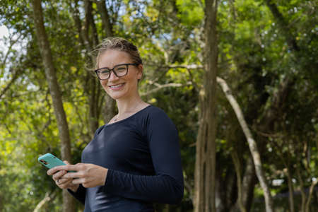 Young woman using a laptop at day time with a green park in the background. High quality photo. Mobile phone, technology, urban concept.の写真素材