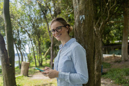 Young woman using a laptop at day time with a green park in the background. High quality photo. Mobile phone, technology, urban concept.の写真素材