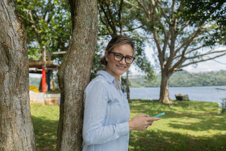 Young woman using a laptop at day time with a green park in the background. High quality photo. Mobile phone, technology, urban concept.の写真素材