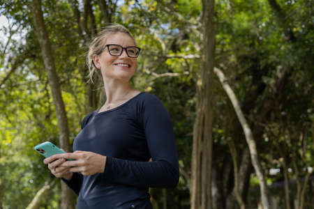 Portrait of smiling young woman at a park on a beautiful sunny day. Woman with open arms in front of a big a tree. Green and nature background. high quality photoの写真素材