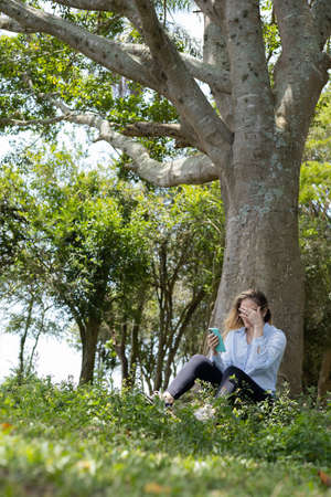 Portrait of smiling young woman at a park on a beautiful sunny day. Woman with open arms in front of a big a tree. Green and nature background. high quality photoの写真素材