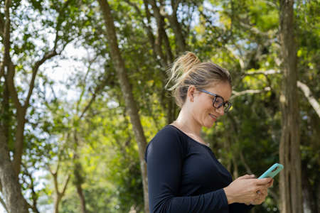 Portrait of smiling young woman at a park on a beautiful sunny day. Woman with open arms in front of a big a tree. Green and nature background. high quality photoの写真素材