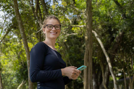 Portrait of smiling young woman at a park on a beautiful sunny day. Woman with open arms in front of a big a tree. Green and nature background. high quality photoの写真素材