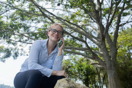 Portrait of smiling young woman at a park on a beautiful sunny day. Woman with open arms in front of...