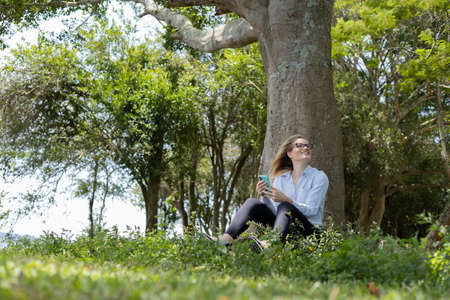 Young woman using a laptop at day time with a green park in the background. High quality photo. Mobile phone, technology, urban concept.の写真素材