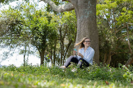 Young woman using a laptop at day time with a green park in the background. High quality photo. Mobile phone, technology, urban concept.の写真素材