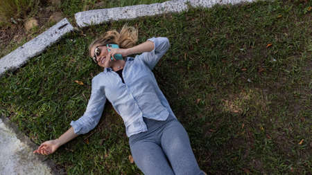 Young woman using a laptop at day time with a green park in the background. High quality photo. Mobile phone, technology, urban concept.の写真素材