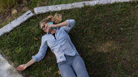 Young woman with sunglasses lyind down on the grass using a smartphone at day time at a green park...