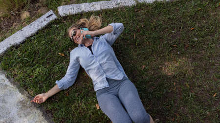 Young woman with sunglasses lyind down on the grass using a smartphone at day time at a green park in the background. High quality photo. Mobile phone, technology, urban concept. high quality photoの写真素材