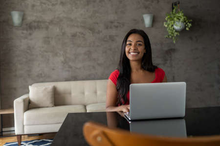 Young black woman working at home with laptop on her lap sitting on her couch in the living room. Home office concept. Gray notebook for working. high quality photoの写真素材