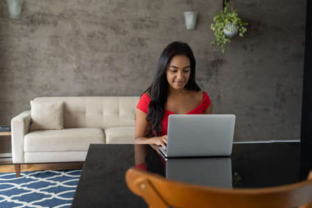 Young black woman working at home with laptop on her lap sitting on her couch in the living room. Home office concept. Gray notebook for working. high quality photoの写真素材