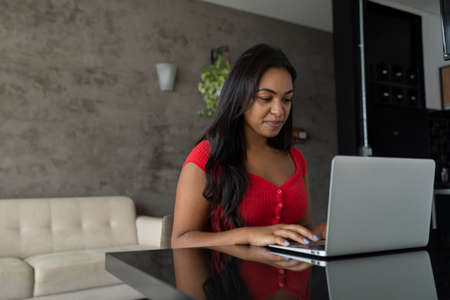 Young black woman working at home with laptop on her lap sitting on her couch in the living room. Home office concept. Gray notebook for working. high quality photoの写真素材