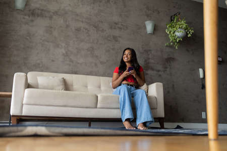 Young black woman working at home with laptop on her lap sitting on her couch in the living room. Home office concept. Gray notebook for working. high quality photoの写真素材