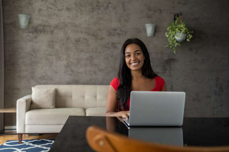 Young black woman working at home with laptop on her lap sitting on her couch in the living room. Home office concept. Gray notebook for working. high quality photoの写真素材