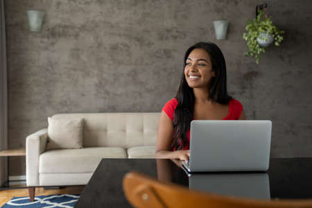 Young black woman working at home with laptop on her lap lying down on her couch in the living room. Home office concept. Gray notebook for working. high quality photoの写真素材