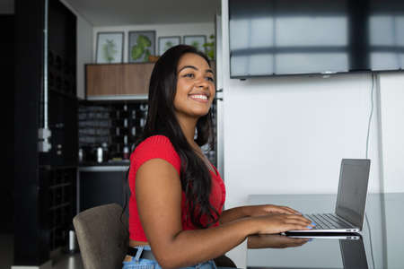Young black woman working at home with laptop on her lap lying down on her couch in the living room....