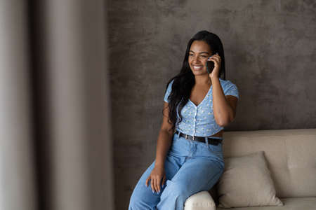 Young black woman working at home with laptop on her lap lying down on her couch in the living room. Home office concept. Gray notebook for working. high quality photoの写真素材