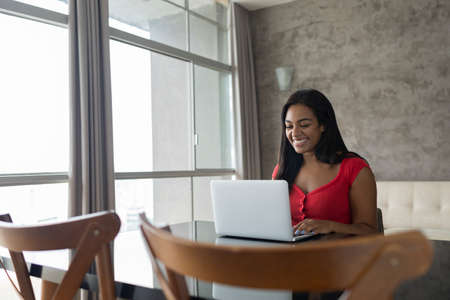 Young black woman working at home with laptop on her lap lying down on her couch in the living room. Home office concept. Gray notebook for working. high quality photoの写真素材