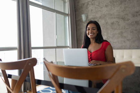 Young black woman working at home with laptop on her lap lying down on her couch in the living room. Home office concept. Gray notebook for working. high quality photoの写真素材