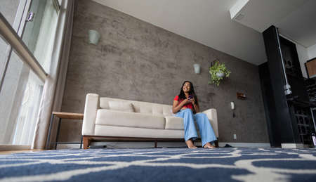 Young black woman working at home with laptop on her lap lying down on her couch in the living room. Home office concept. Gray notebook for working. high quality photoの写真素材