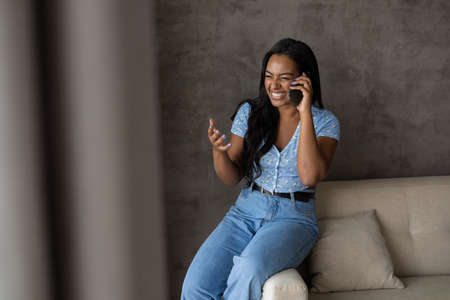 Young black woman working at home with laptop on her lap lying down on her couch in the living room. Home office concept. Gray notebook for working. high quality photoの写真素材