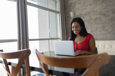 Young black woman working at home with laptop on her lap lying down on her couch in the living room. Home office concept. Gray notebook for working. high quality photoの写真素材