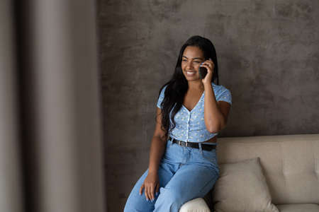 Young black woman working at home with laptop on her lap lying down on her couch in the living room. Home office concept. Gray notebook for working. high quality photoの写真素材