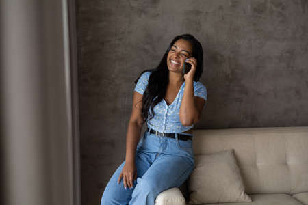 Young black woman working at home with laptop on her lap lying down on her couch in the living room. Home office concept. Gray notebook for working. high quality photoの写真素材