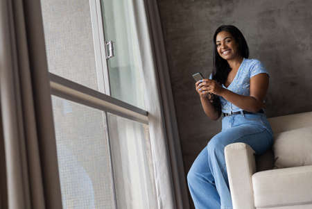 Young black woman working at home with laptop on her lap lying down on her couch in the living room. Home office concept. Gray notebook for working. high quality photoの写真素材