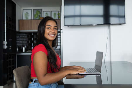 Young black woman working at home with laptop on her lap lying down on her couch in the living room. Home office concept. Gray notebook for working. high quality photoの写真素材