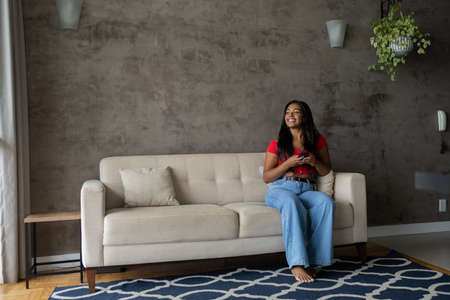 Young black woman working at home with laptop on her lap lying down on her couch in the living room. Home office concept. Gray notebook for working. high quality photoの写真素材