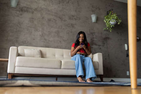 Young black woman working at home with laptop on her lap lying down on her couch in the living room. Home office concept. Gray notebook for working. high quality photoの写真素材