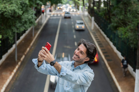 View of a young man with smartphone at daytime with traffic and cars landscape in the background. Taking a selfie - video call with smartphone. High quality photo.の写真素材