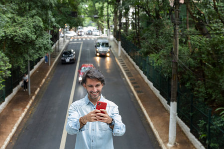 View of a young man with smartphone at daytime with traffic and cars landscape in the background. Taking a selfie - video call with smartphone. High quality photo.の写真素材
