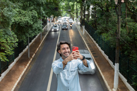 View of a young man with smartphone at daytime with traffic and cars landscape in the background. Taking a selfie - video call with smartphone. High quality photo.の写真素材