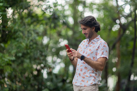 View of a young man with smartphone at daytime in a green park in the city. High quality photo.の写真素材