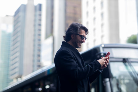 View of a well dressed young man with sunglasses and smartphone at daytime with city view landscape in the background. High quality photo.の写真素材