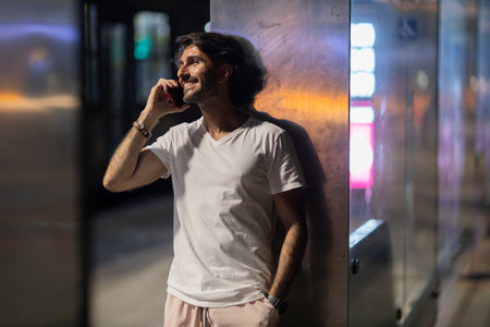View of young man using a smartphone at night time with city view landscape in the background. High...