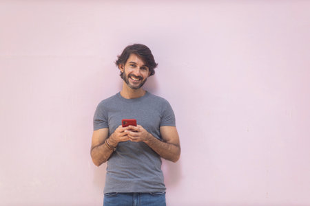 View of a young man with smartphone at daytime on pink wall in the city. High quality photo.の写真素材