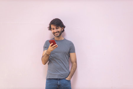 View of a young man with smartphone at daytime on pink wall in the city. High quality photo.の写真素材